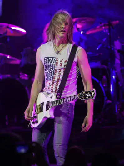 Guitarist performing live on stage with electric guitar under purple stage lighting
