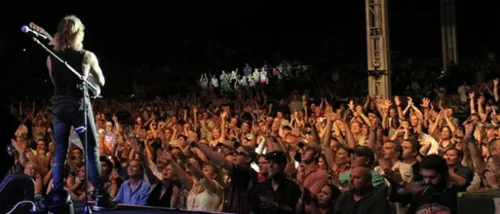 Musician performing at microphone on stage with large audience with hands raised
