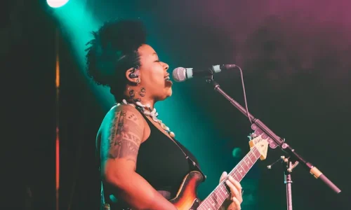 Female musician performing with guitar and microphone on stage with teal and amber lighting